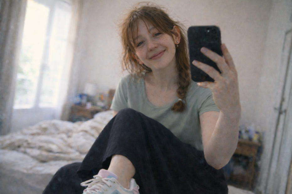 Jeune femme aux taches de rousseur prenant un selfie miroir dans une chambre, portant des baskets coréennes et une jupe longue noire, lumière naturelle imparfaite.