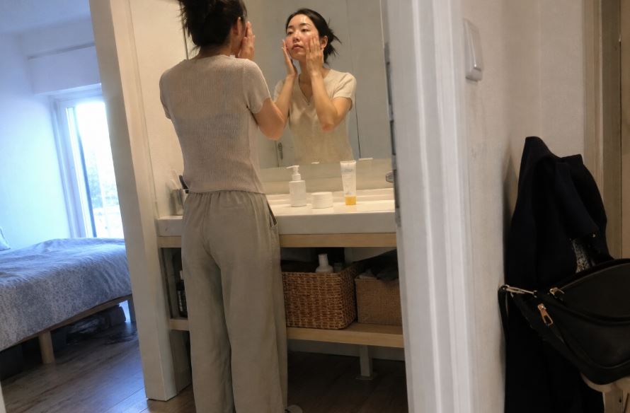 Jeune femme asiatique appliquant une protection solaire devant son miroir avec trois soins essentiels