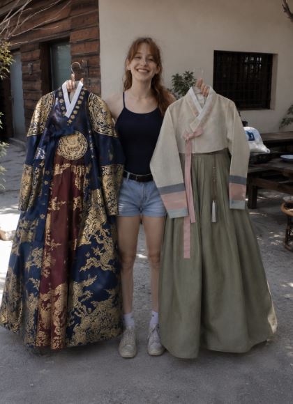 Jeune femme tenant deux hanboks coréens différents, un hanbok royal bleu et or et un hanbok populaire traditionnel vert pastel, photo casual réaliste.