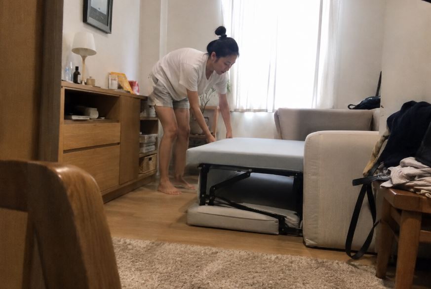 Jeune femme préparant un canapé convertible compact dans une petite chambre d’amis avec rangements en bois clair