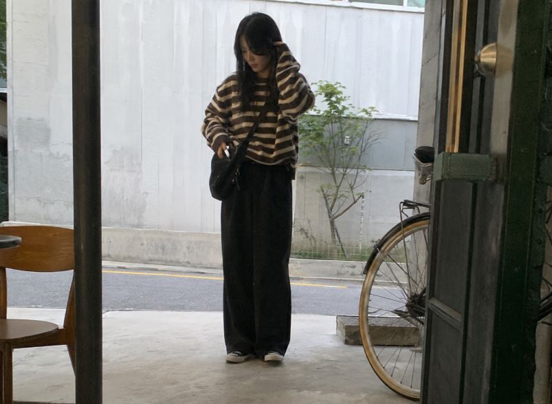 Jeune femme asiatique portant un pull rayé oversize bleu marine et écru avec un pantalon beige dans une rue de Séoul