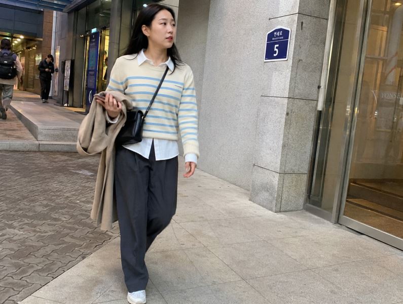 Jeune femme asiatique portant un pull rayé oversize bleu marine et écru avec un pantalon beige dans une rue de Séoul