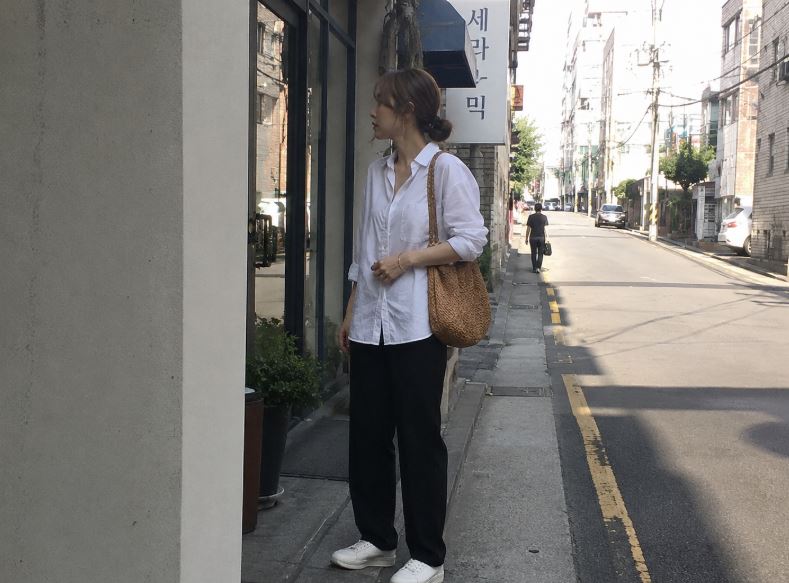 Jeune femme asiatique portant une chemise blanche, un pantalon noir et un sac bohème brun en raphia dans une rue de Séoul