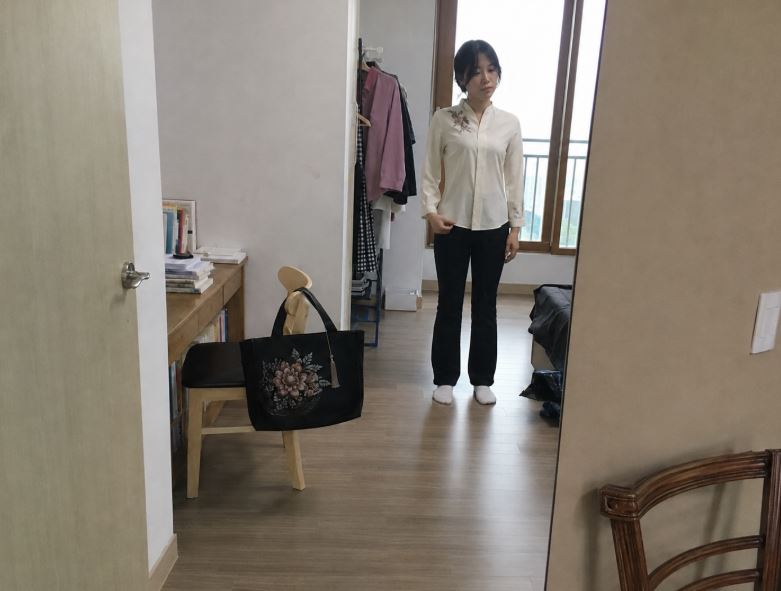 Jeune femme essayant une blouse crème ornée d’une broderie de pivoine dans un appartement