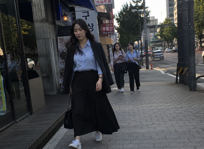 Femme asiatique en jupe longue noire, chemise bleu clair et blazer dans une rue de Séoul