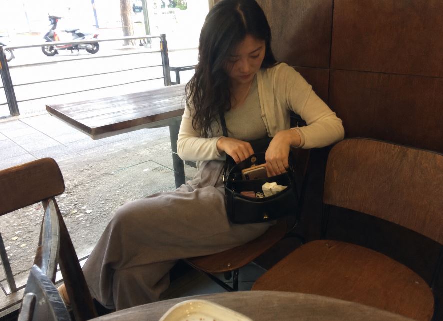 Jeune femme assise dans un café à Séoul avec un petit sac bandoulière ouvert contenant téléphone, portefeuille et objets du quotidien