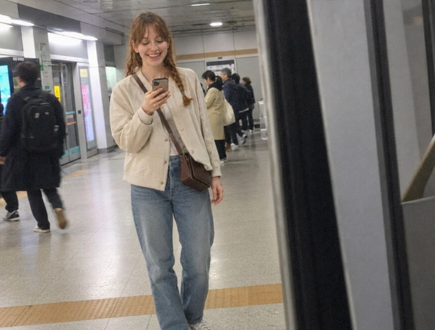 jeune femme dans le métro de Séoul portant un petit sac bandoulière brun en travers du corps tout en consultant son téléphone