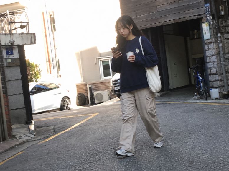 Jeune femme portant un sweat brodé gris clair avec chemise blanche et pantalon de tailleur anthracite dans un café à Séoul