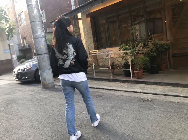 Jeune femme portant une veste moderne avec une grue brodée dans le dos dans une rue de Séoul